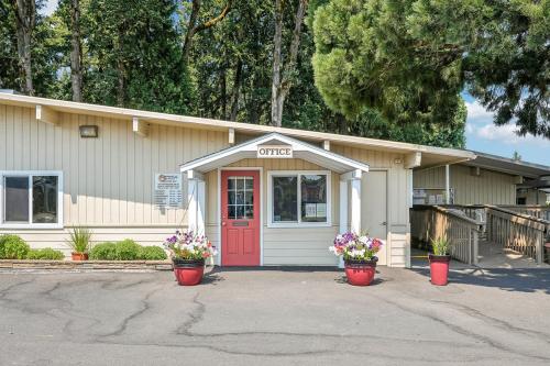 A beige building with a red door marked "Office." Two red potted plants flank the entrance. Trees are visible in the background.