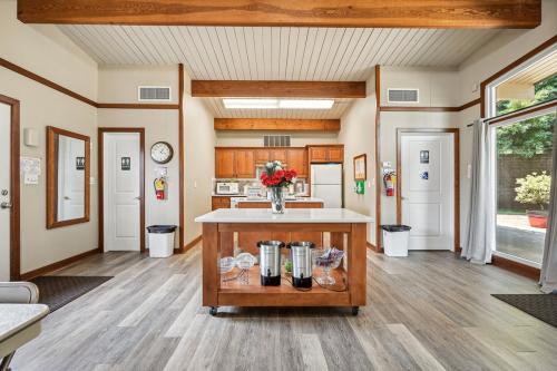 A spacious kitchen with wooden beams on the ceiling, featuring a central island with dispensers, and a well-lit area with modern appliances and large windows allowing natural light to enter.